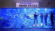 鳥羽水族館で恒例の「水中入社式」、スーツ姿の新入社員が水槽内で辞令書を受け取る